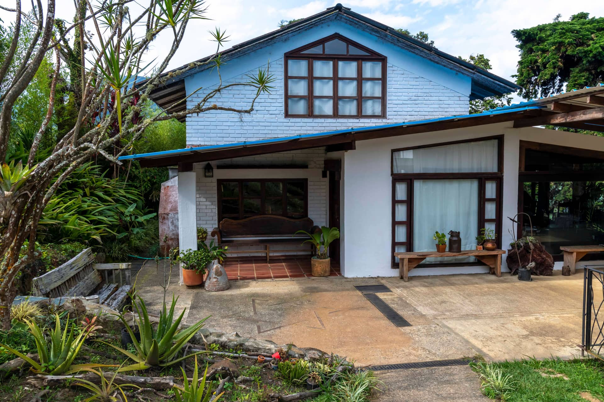 Fachada de Casa Maima con techo azul, terraza de piedra y jardín de plantas tropicales