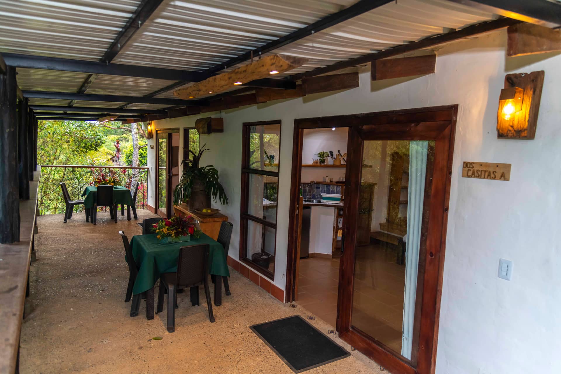 Terraza cubierta de Dos Casitas con mesas de comedor y la entrada a los alojamientos