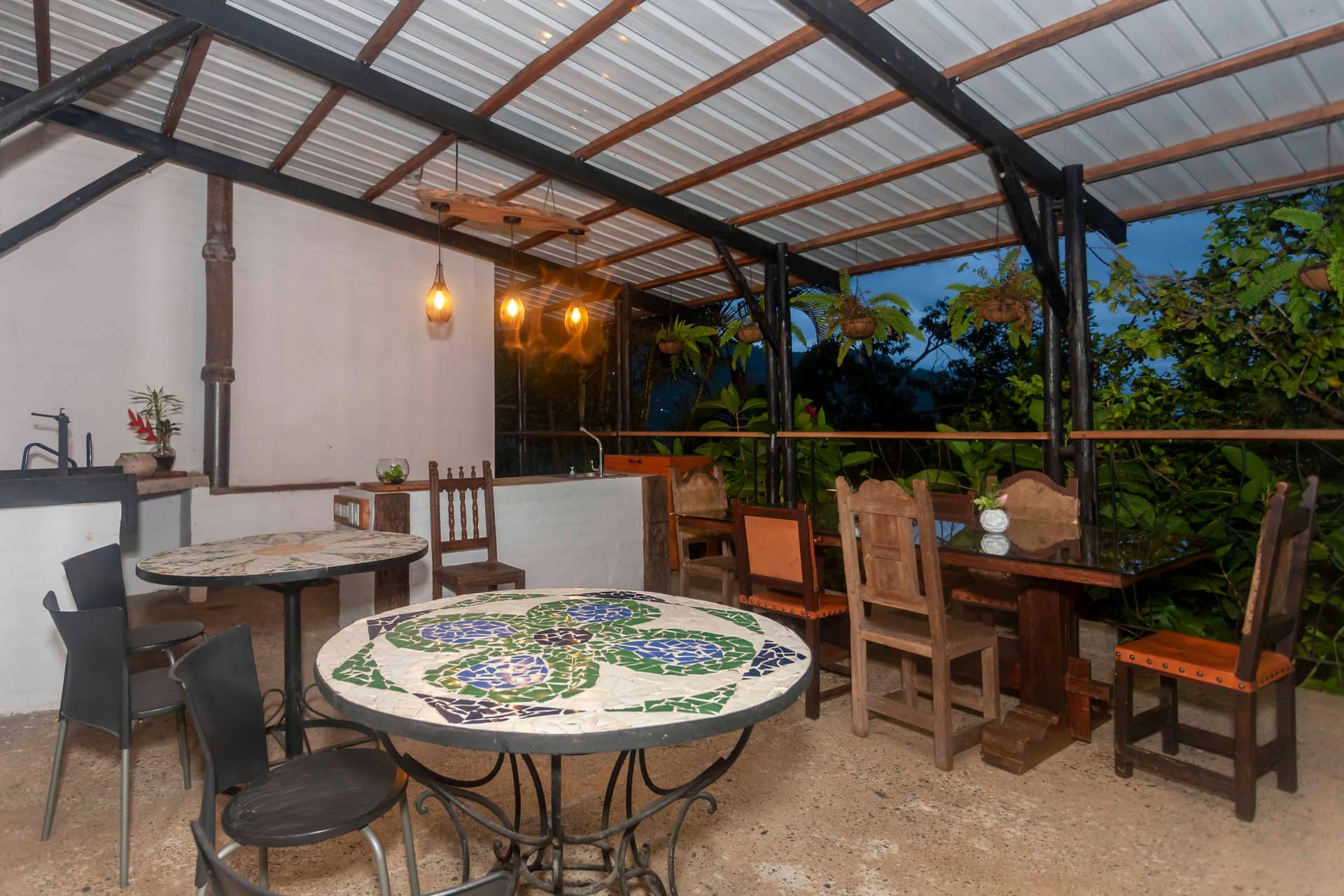 Comedor de La Maima bajo la pérgola al atardecer, con mesas de mosaico y sillas de madera